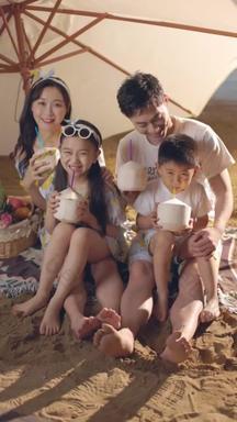 快乐的四口之家坐在沙滩上喝椰汁